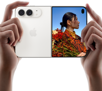 iPhone Duo, Star White colour, held by two hands in horizontal orientation, unfolded, left panel shows 48MP Dual Fusion rear cameras, right panel shows person getting their picture taken on outer display, the subject of the photo is able to see their face as their picture is getting taken using Duo Preview