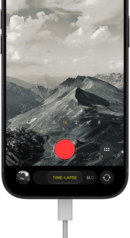 iPhone 18 Pro, front exterior, displaying a mountainous landscape, with the camera mode overlay in Time-Lapse mode, with power cord attached to charging port