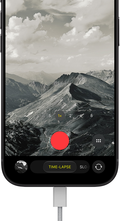 iPhone 18 Pro, front exterior, displaying a mountainous landscape, with the camera mode overlay in Time-Lapse mode, with power cord attached to charging port